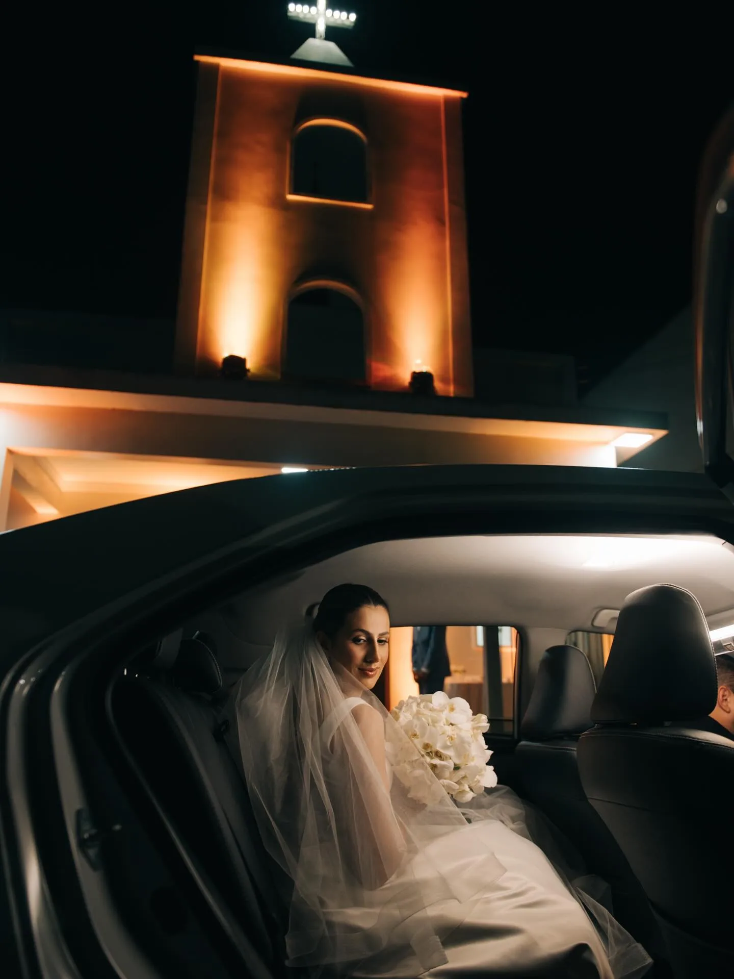 Noiva dentro de um carro diante de igreja iluminada