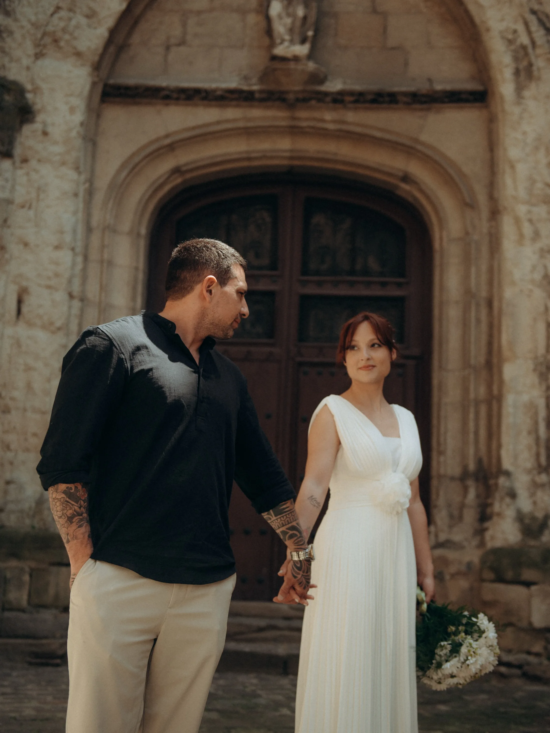 Casal com roupas claras e escuras diante de uma porta antiga