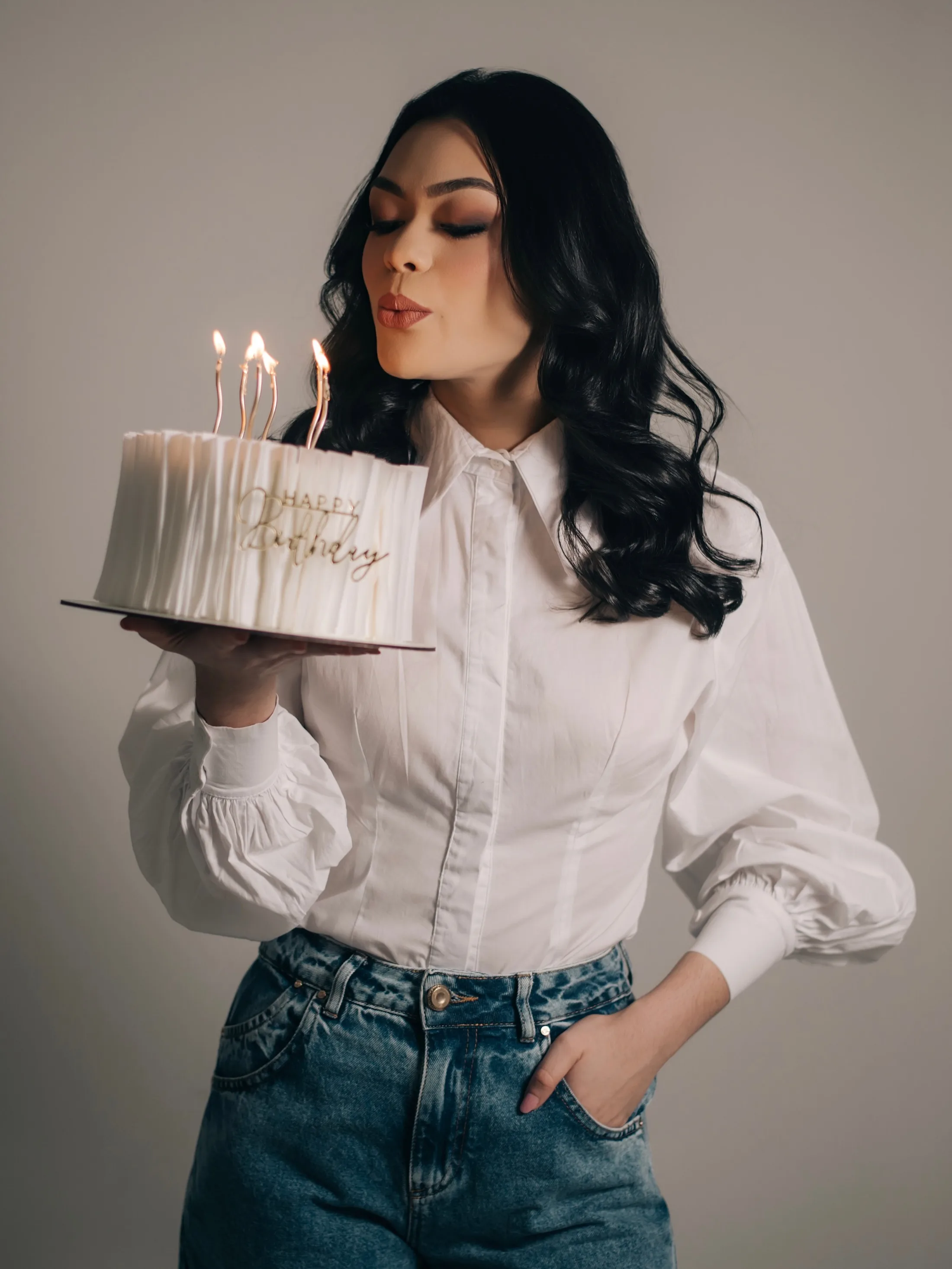 Mulher com camisa clara aproximando o rosto de um bolo
