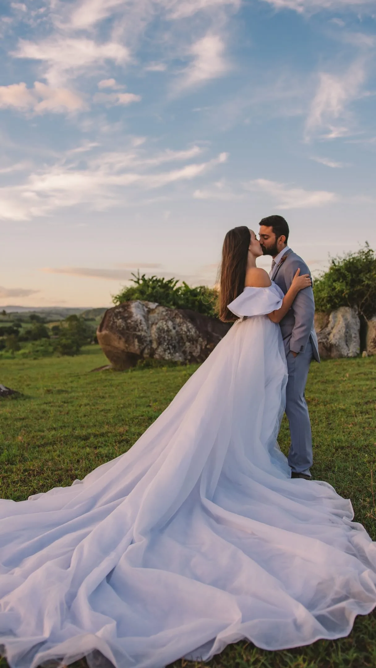 Casal em gramado sob céu colorido ao entardecer