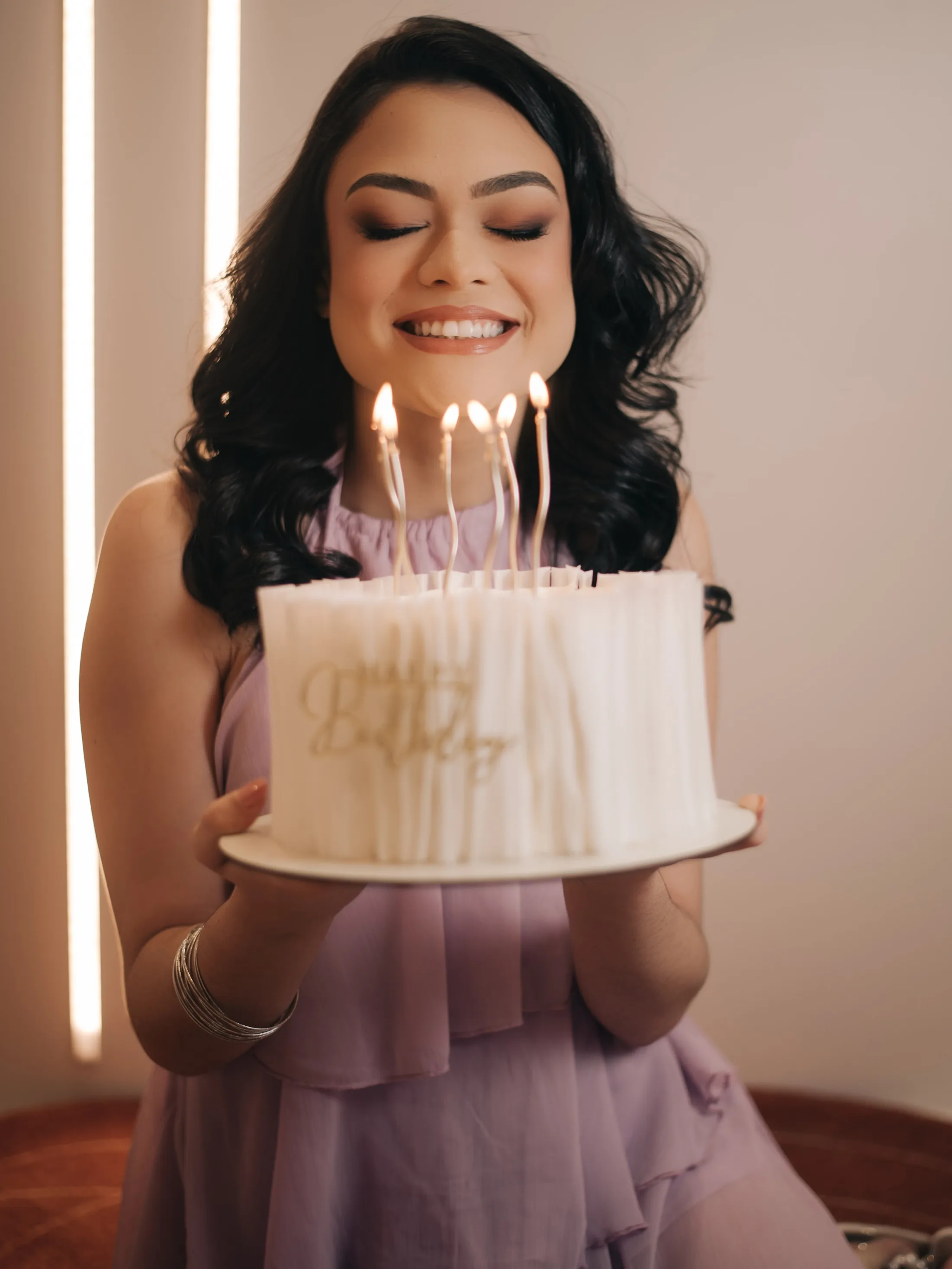 Mulher sorrindo atrás de um bolo com velas acesas