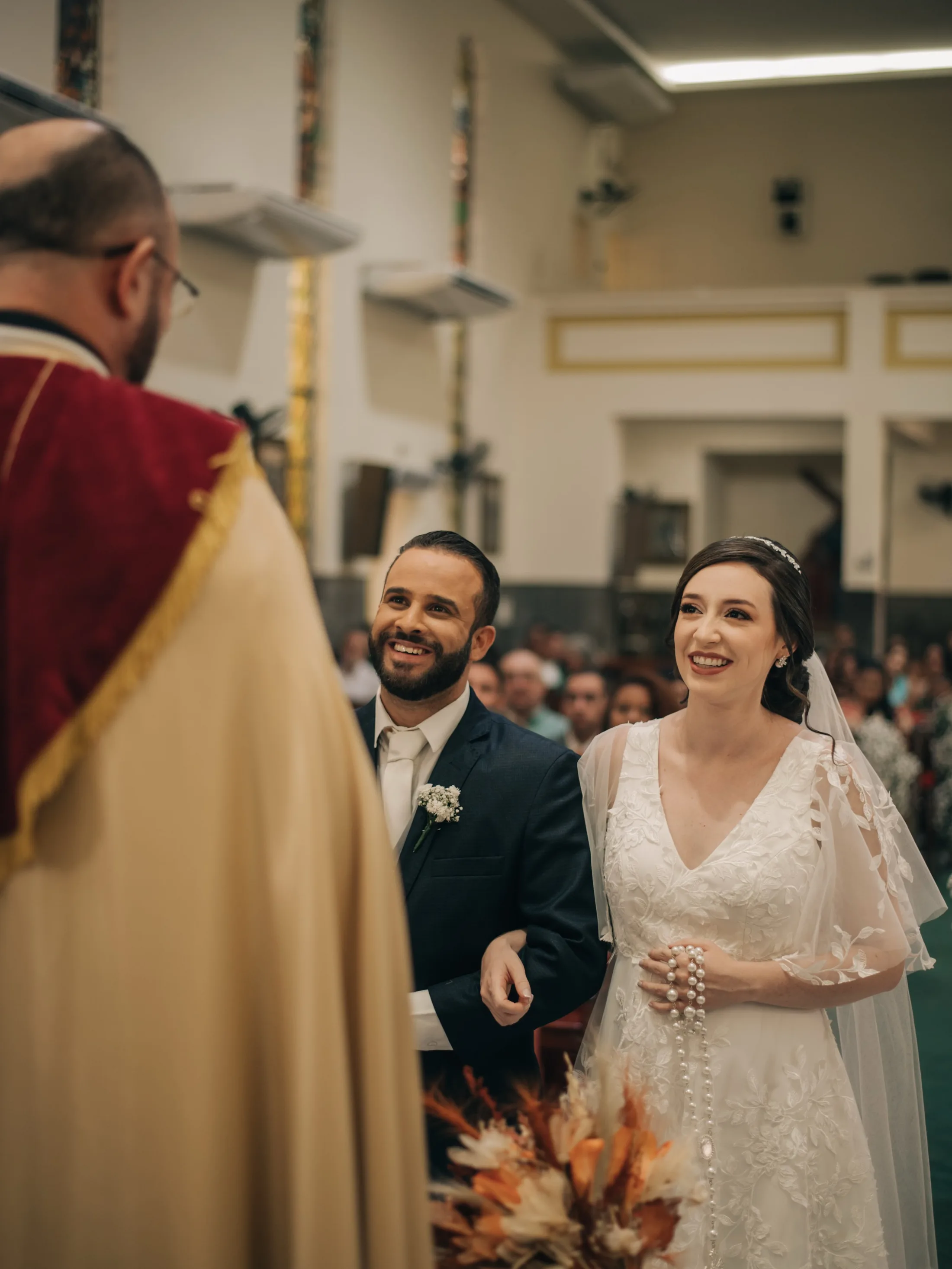 Noivos sorrindo diante do celebrante na igreja